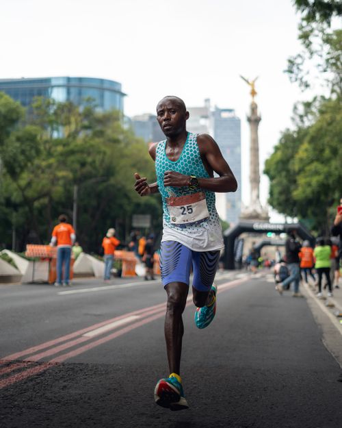 Free Focused runner participating in an urban marathon near a city landmark with support staff in the background. Stock Photo