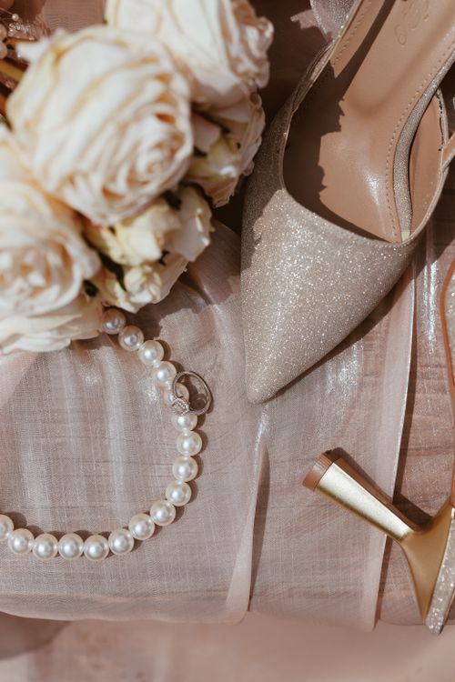 Free Flat lay of elegant wedding shoes, pearl necklace, and roses on satin fabric. Stock Photo