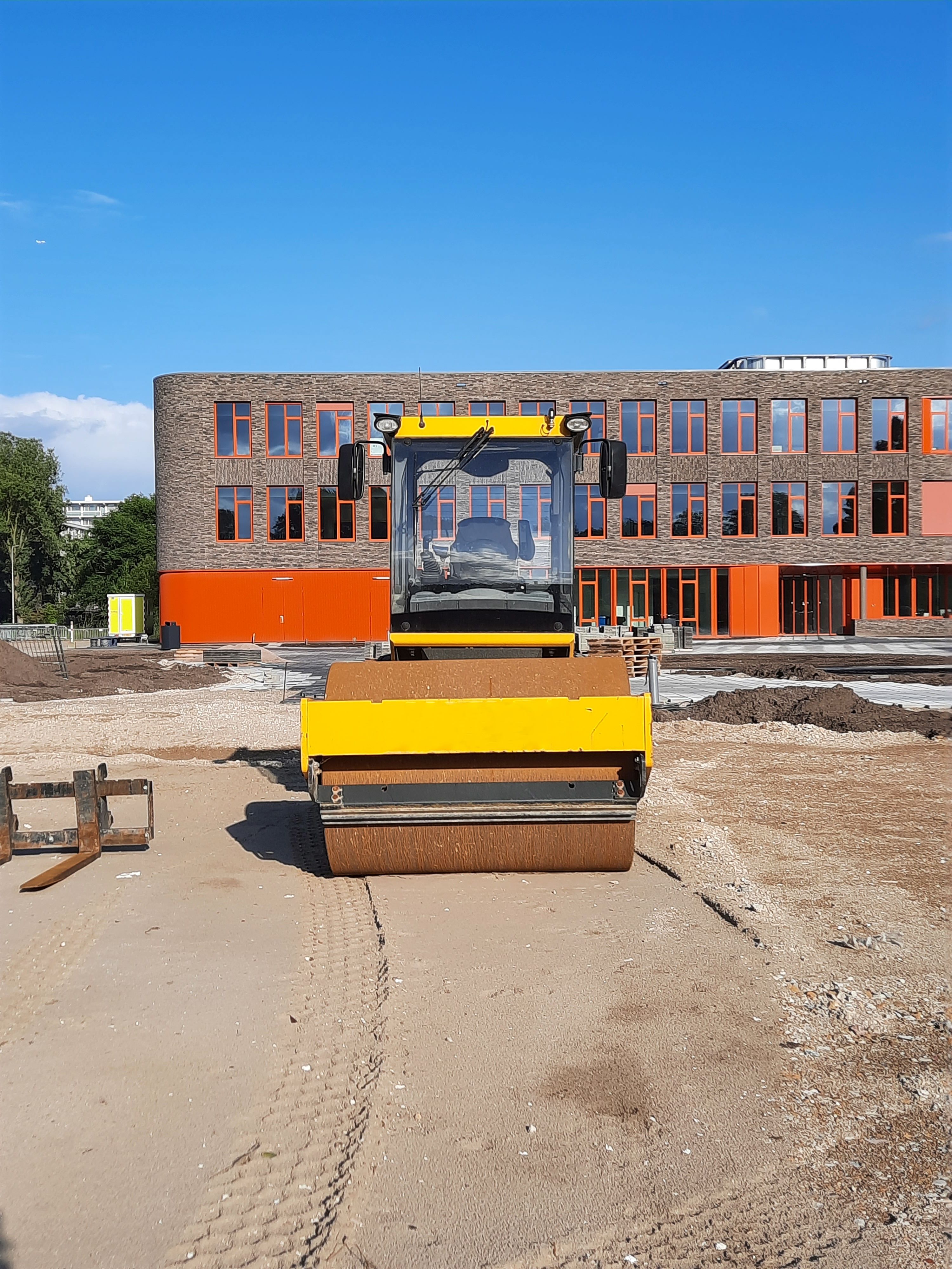 Yellow roller at construction site in front of modern building.
