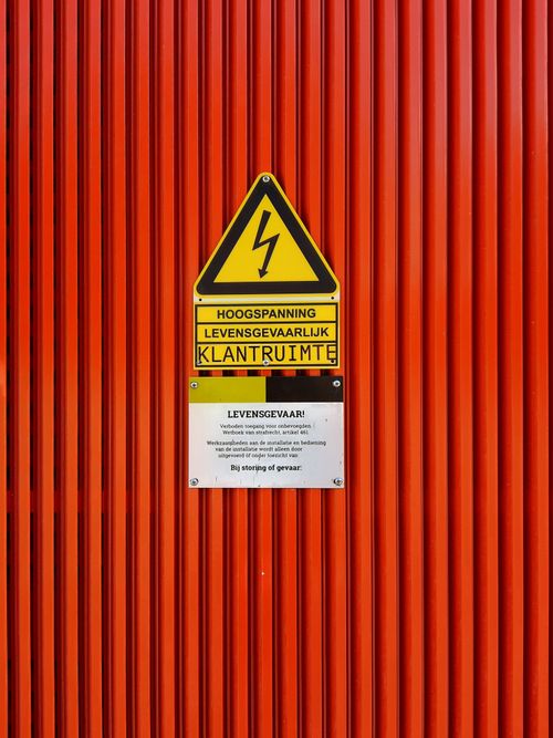 Free Close-up of a warning sign indicating high voltage on a vibrant red striped surface, emphasizing safety. Stock Photo