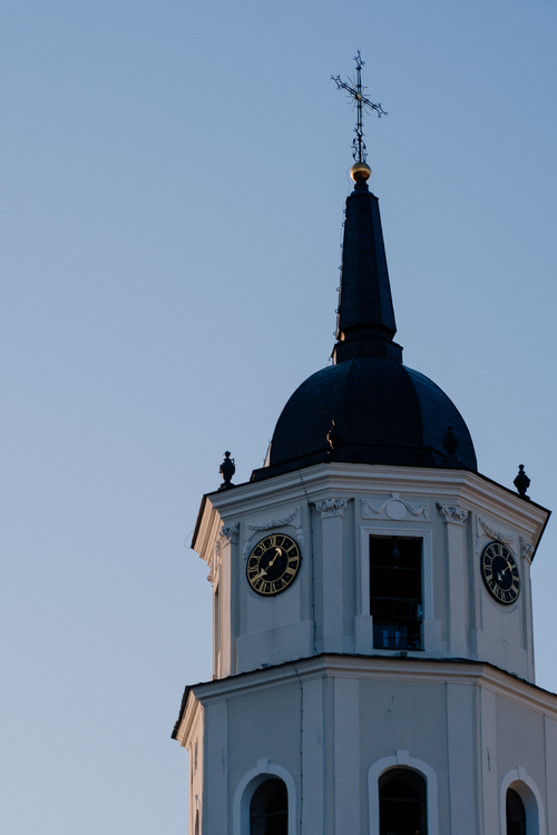 Free A Gothic church tower in Vilnius, Lithuania, at sunset. Cross and clock visible. Stock Photo