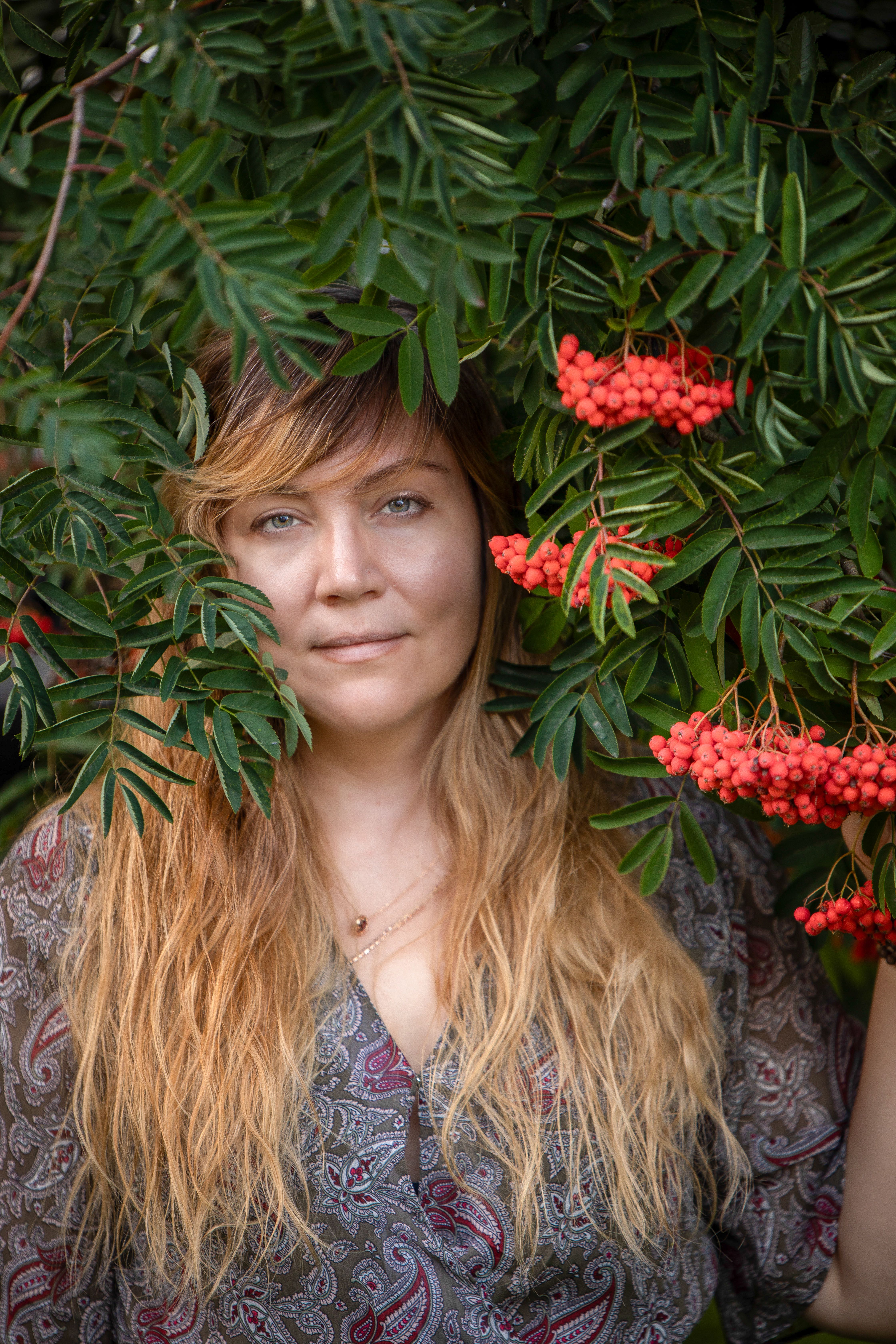 A serene portrait of a woman surrounded by lush green leaves and vibrant red berries.