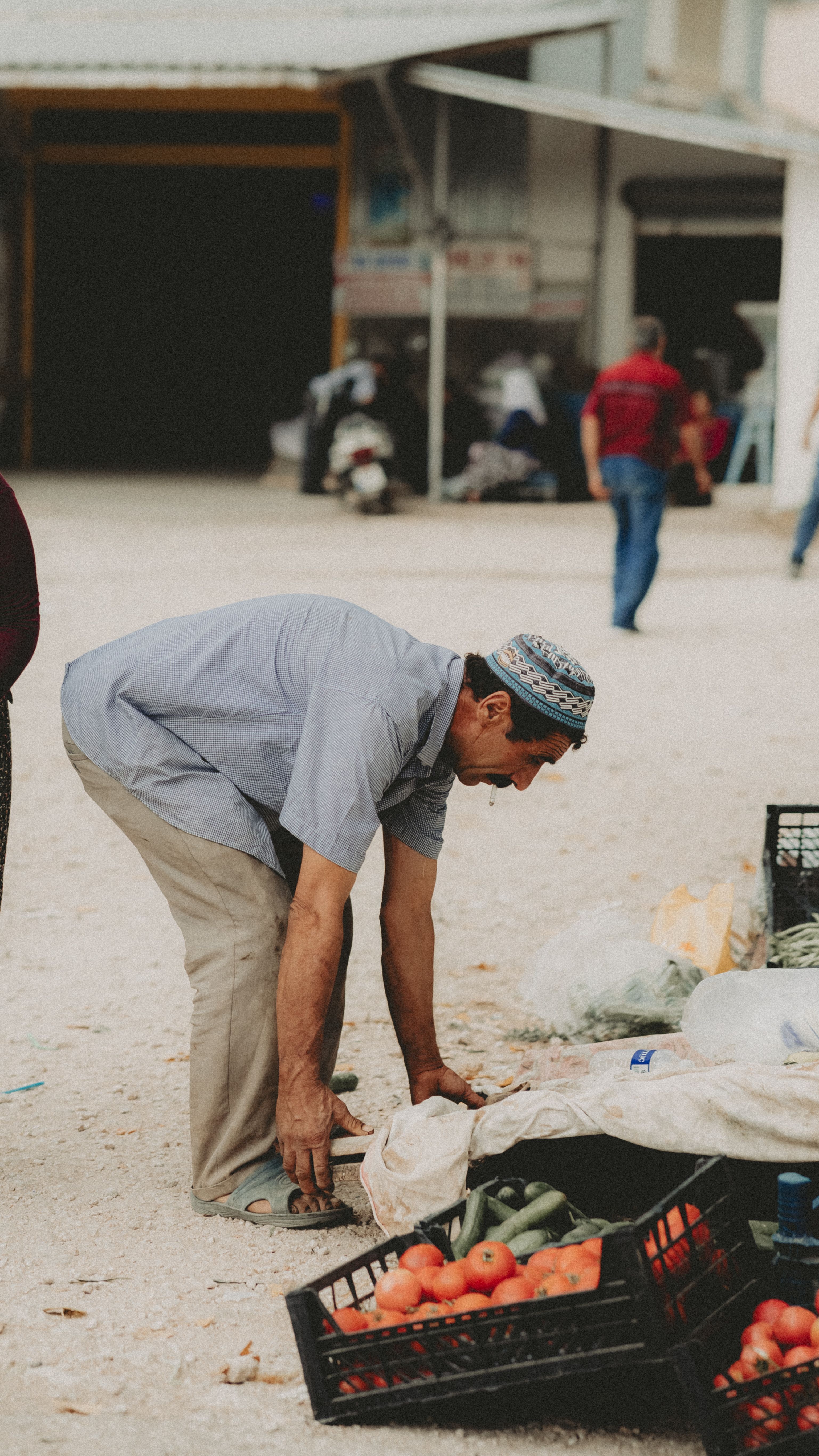 Adult man arranging vegetables at market stall outdoors.