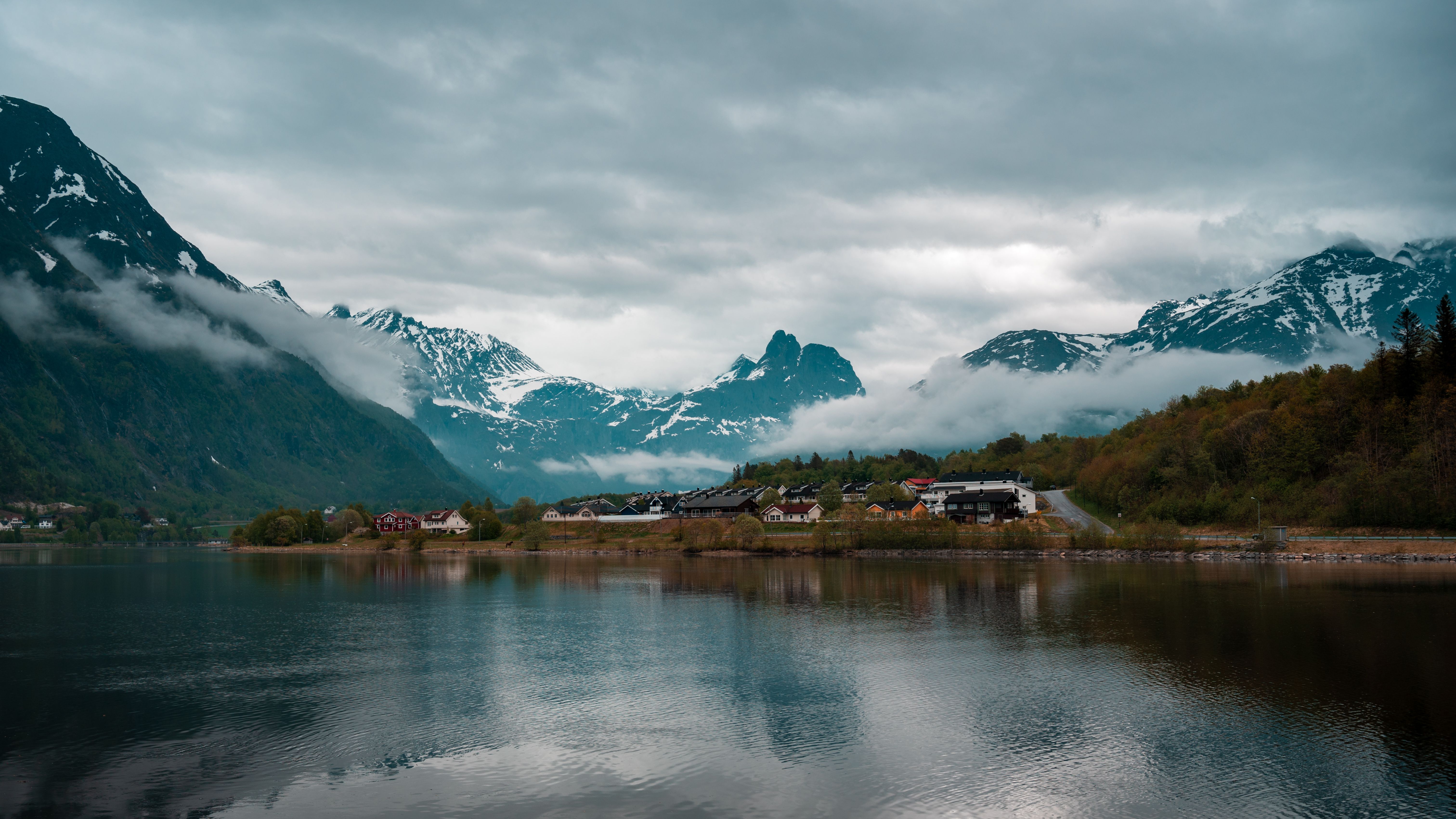 Scenic view of Åndalsnes fjords with houses and snow-capped mountains under a cloudy sky.