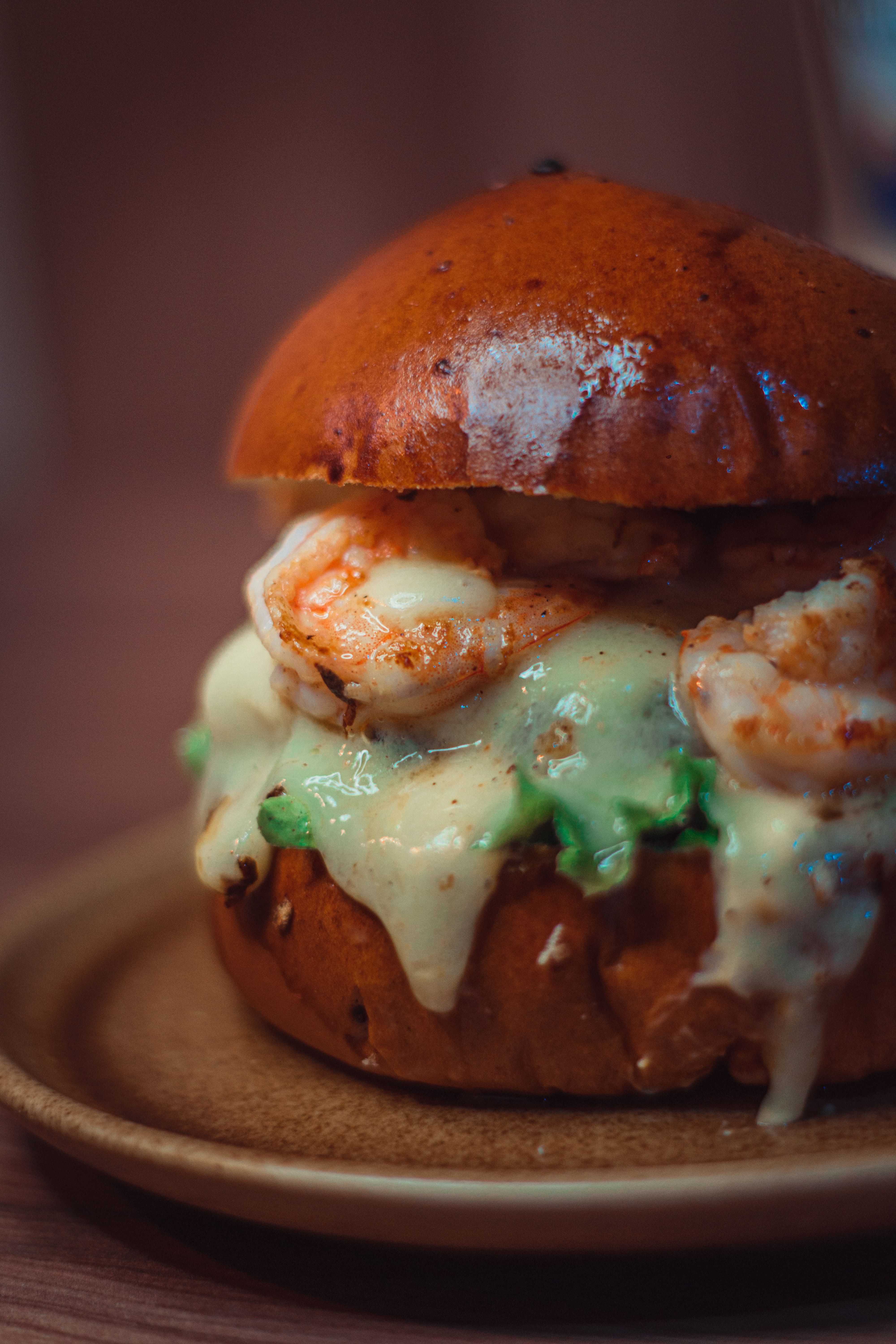 Delicious shrimp burger topped with creamy melted cheese on a wooden plate.