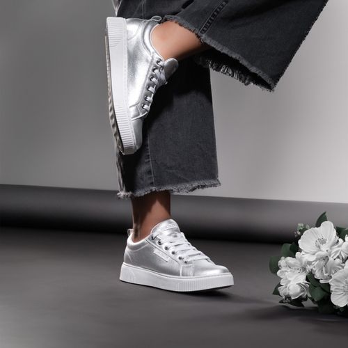 Free Featuring a woman in trendy silver sneakers against an elegant grey backdrop. Stock Photo