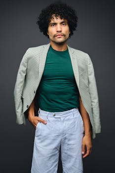 Portrait of a fashionable man with curly hair in a studio setting, wearing a green shirt and suit jacket.