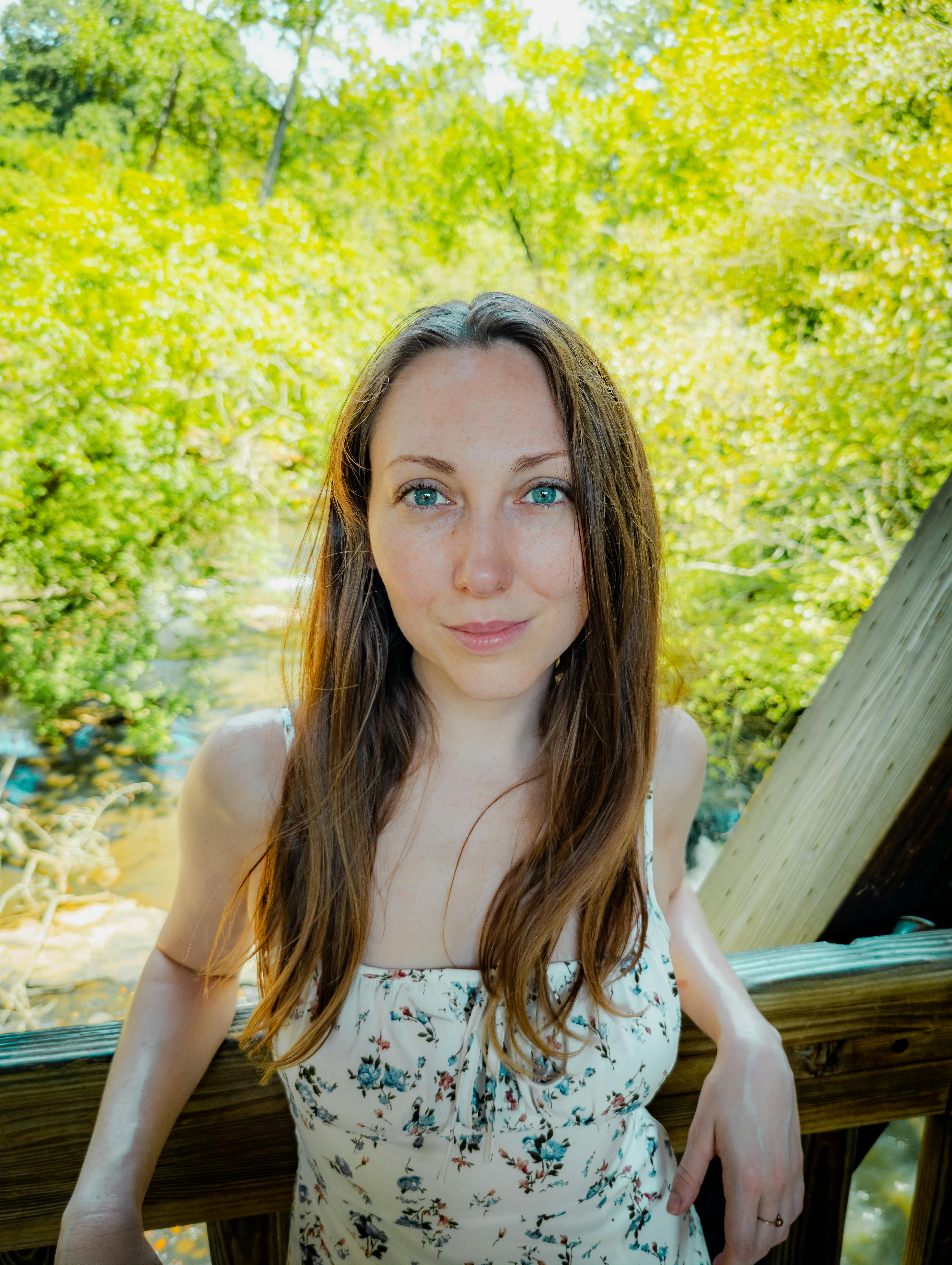 A young woman smiles in a sunlit park, surrounded by greenery, enjoying a summer day.