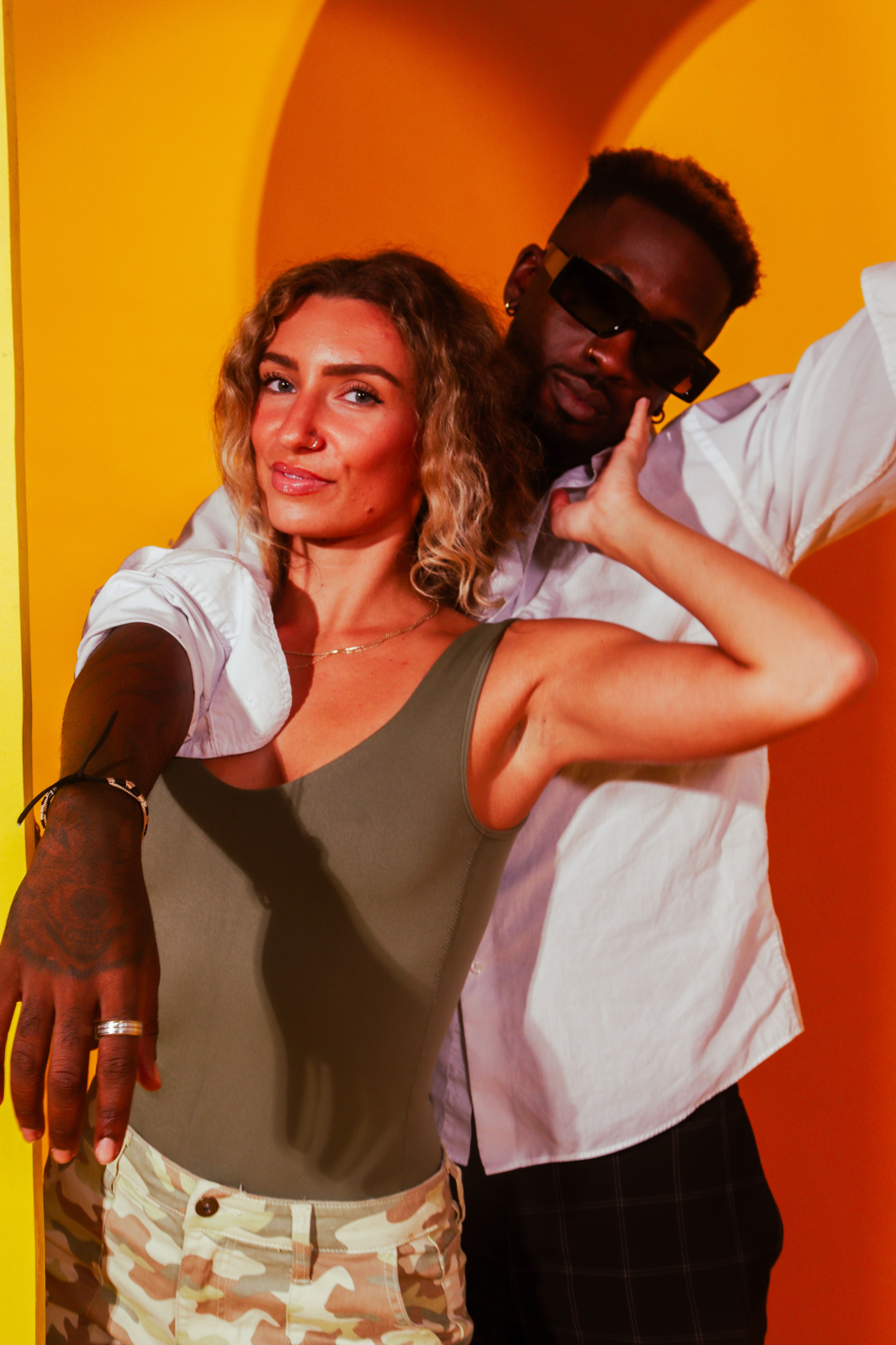 A fashionable couple posing playfully against a vibrant yellow backdrop, exuding joy and confidence.