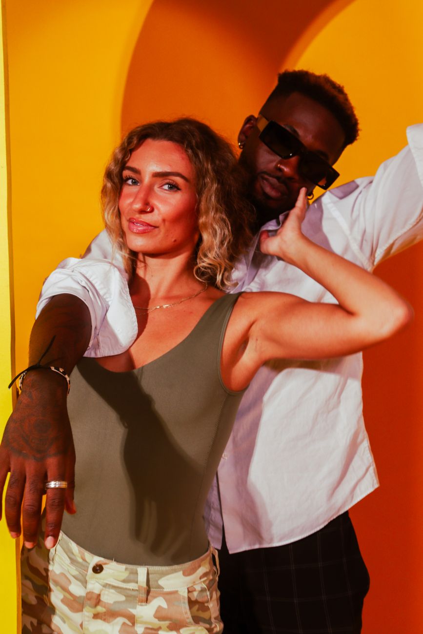 A fashionable couple posing playfully against a vibrant yellow backdrop, exuding joy and confidence.