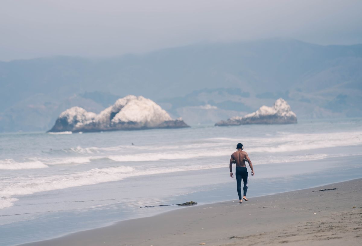 A walker on a foggy stretch of Ocean Beach with sea stacks in the distance