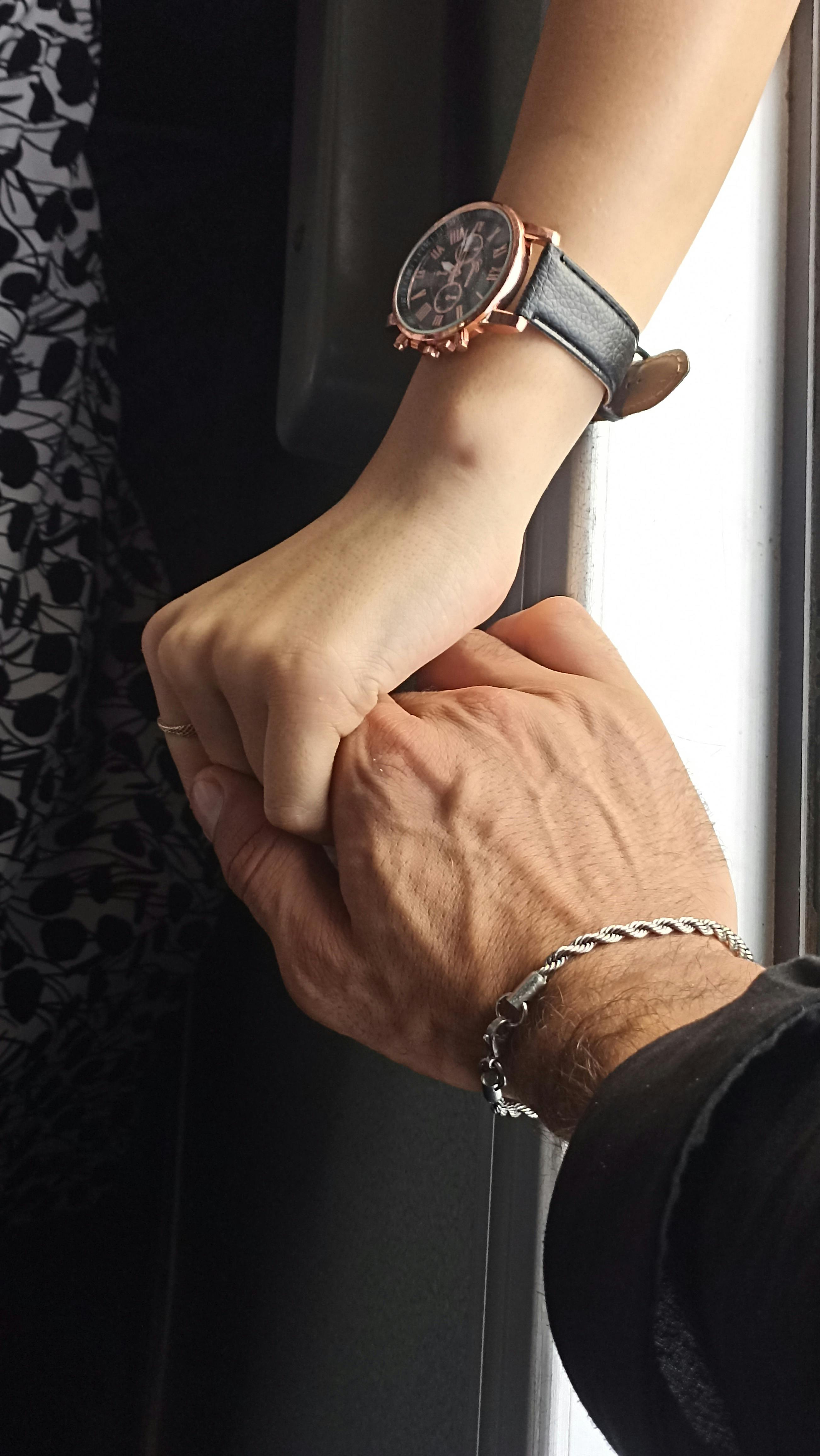 a man and woman holding hands while looking at a watch