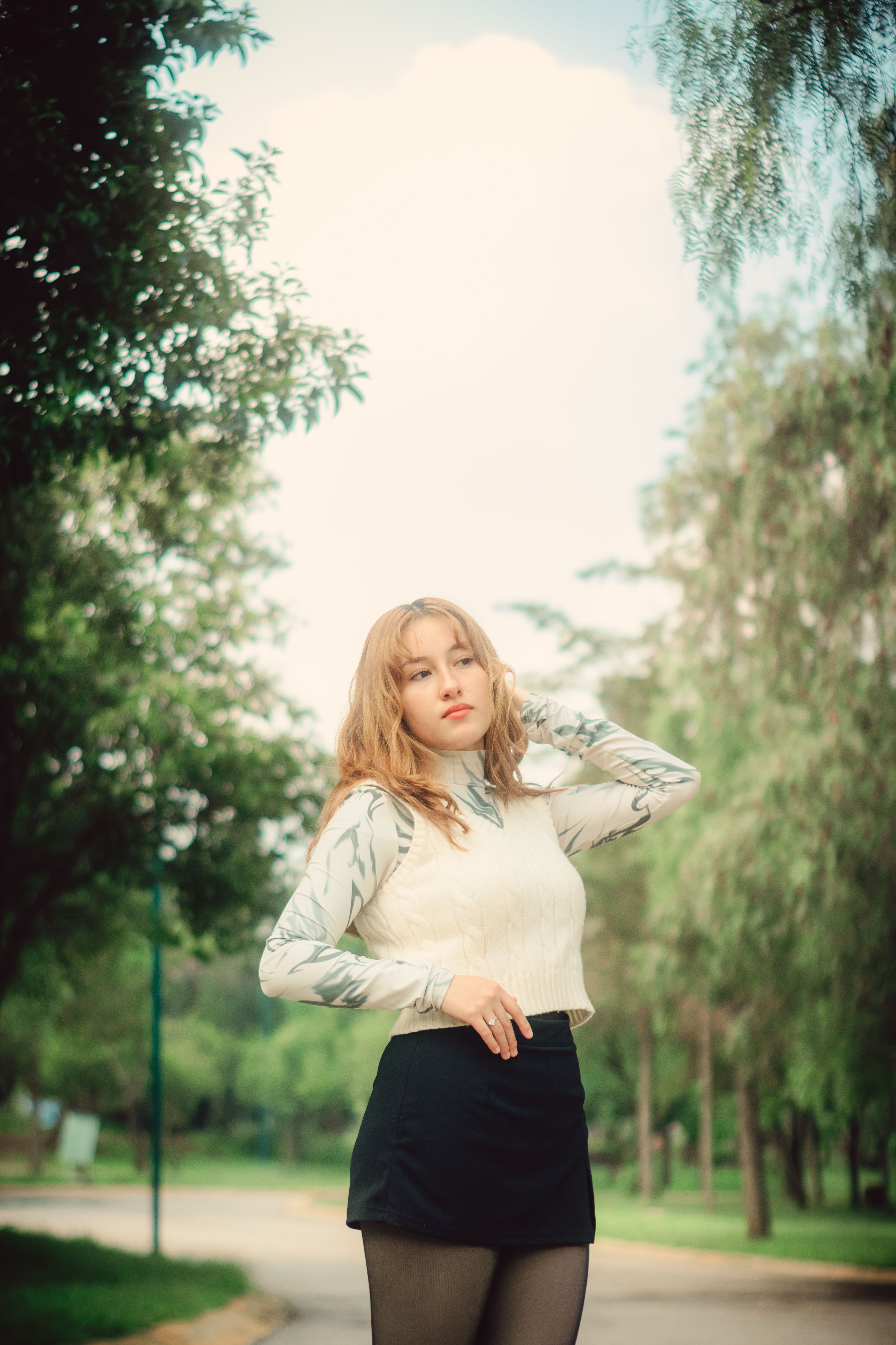 Stylish young woman poses confidently in a lush green park setting.