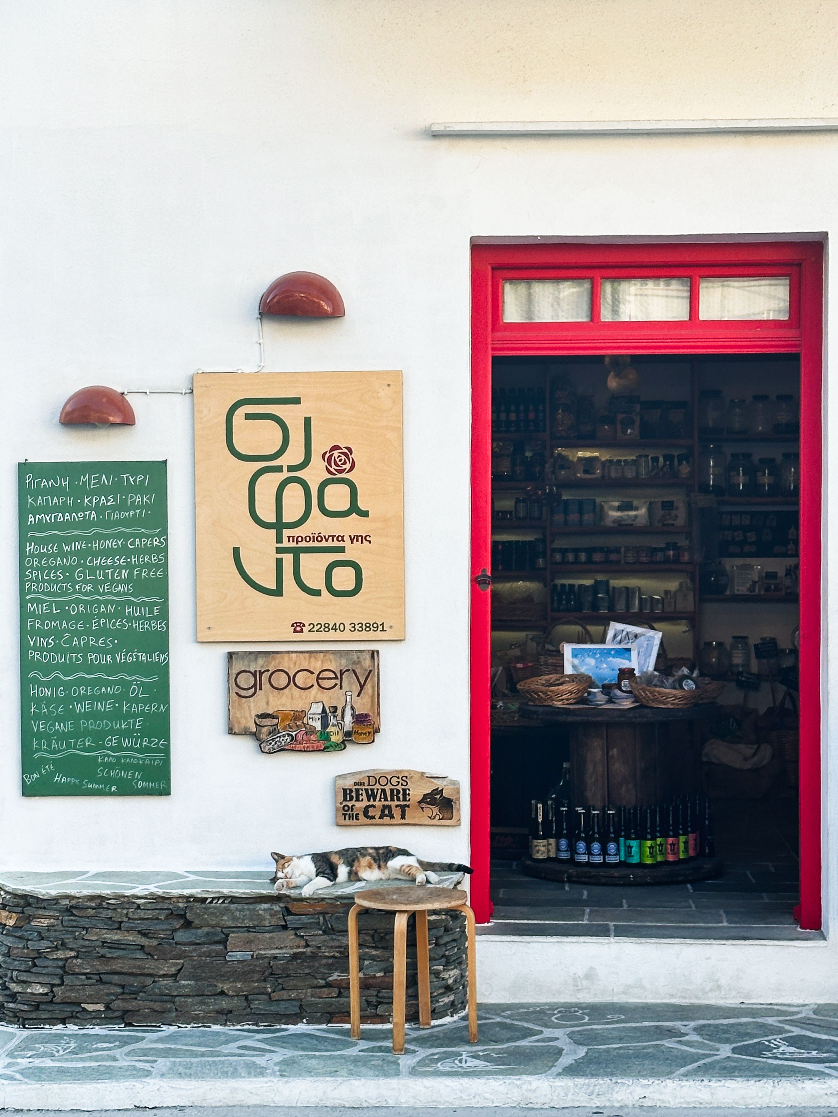 Cozy grocery shop entrance in Greece featuring local produce and a resting cat.