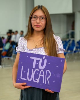 A young woman inside an auditorium holding a sign with 'Tú Lugar' written on it.