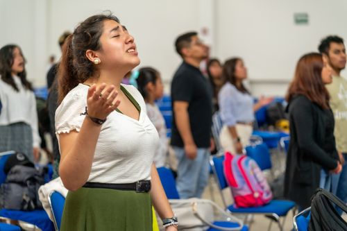 Free Young adults engaged in a worship celebration indoors, raising hands in prayer. Stock Photo