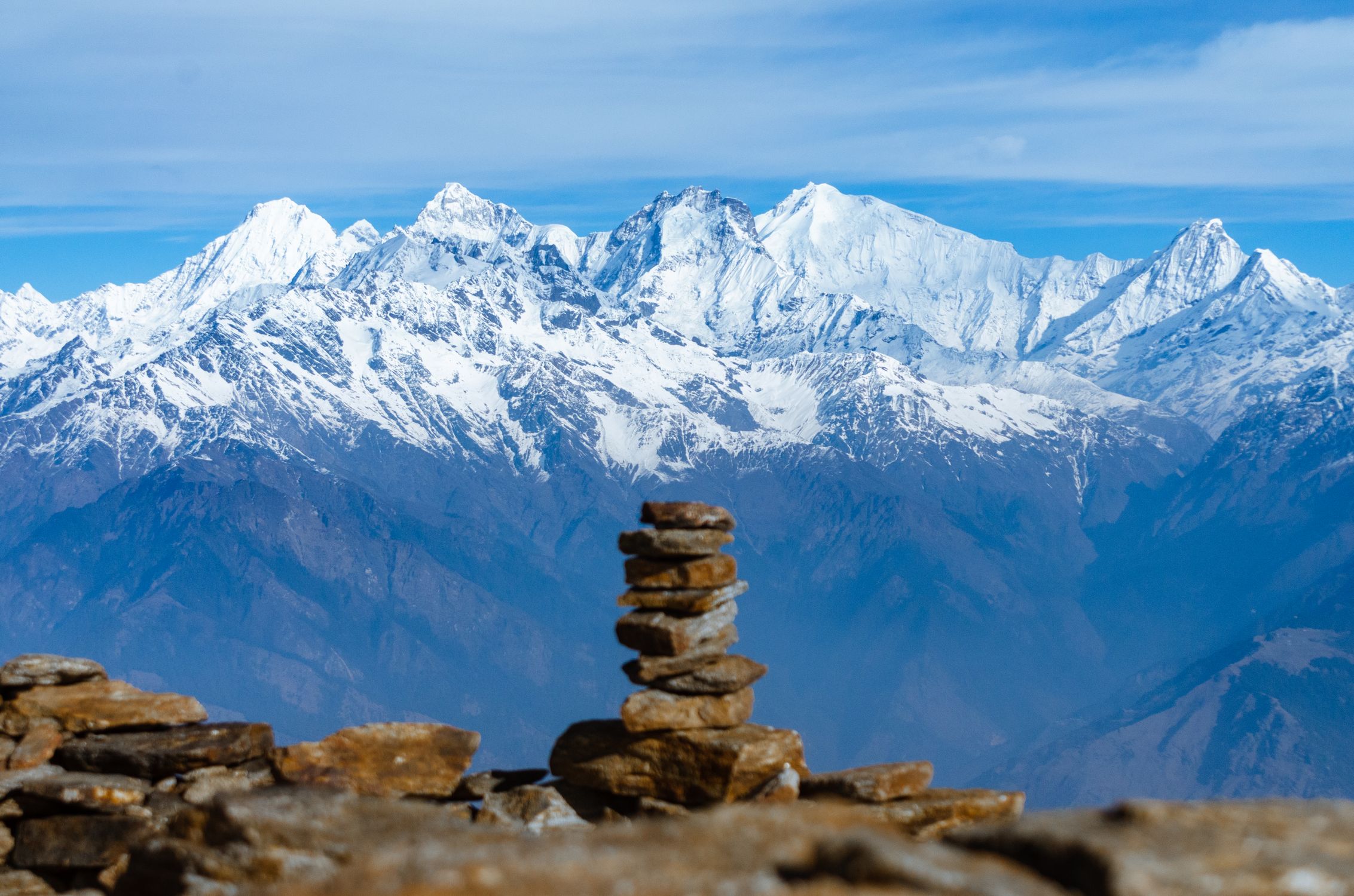 A stack of rocks on top of a mountain with snow capped mountains in the ...