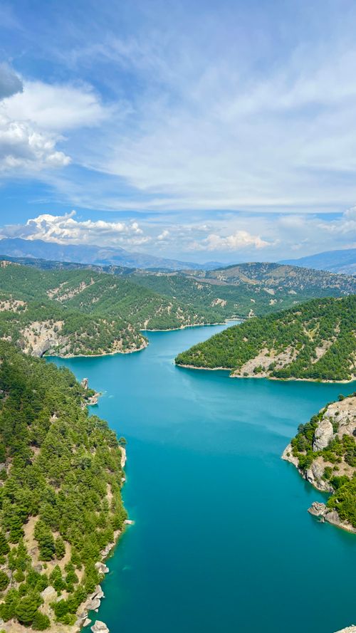 Free A stunning aerial view of a turquoise river meandering through lush green mountains under a blue sky. Stock Photo