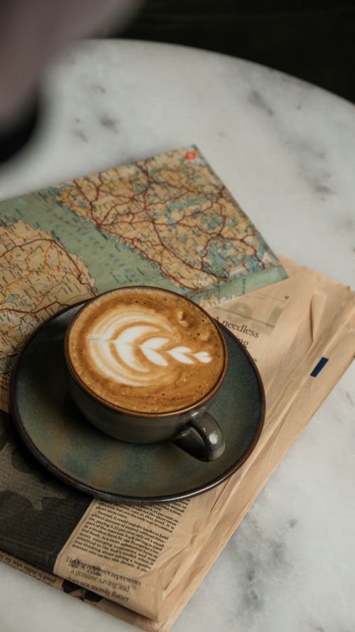 Free Artistic cappuccino on newspapers and a map, perfect for travel inspiration. Stock Photo