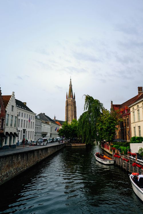 Free Picturesque view of Bruges canal with boats and prominent belfry tower, a classic European cityscape. Stock Photo