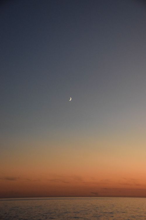 Free Tranquil twilight scene with the crescent moon over a calm ocean horizon. Stock Photo