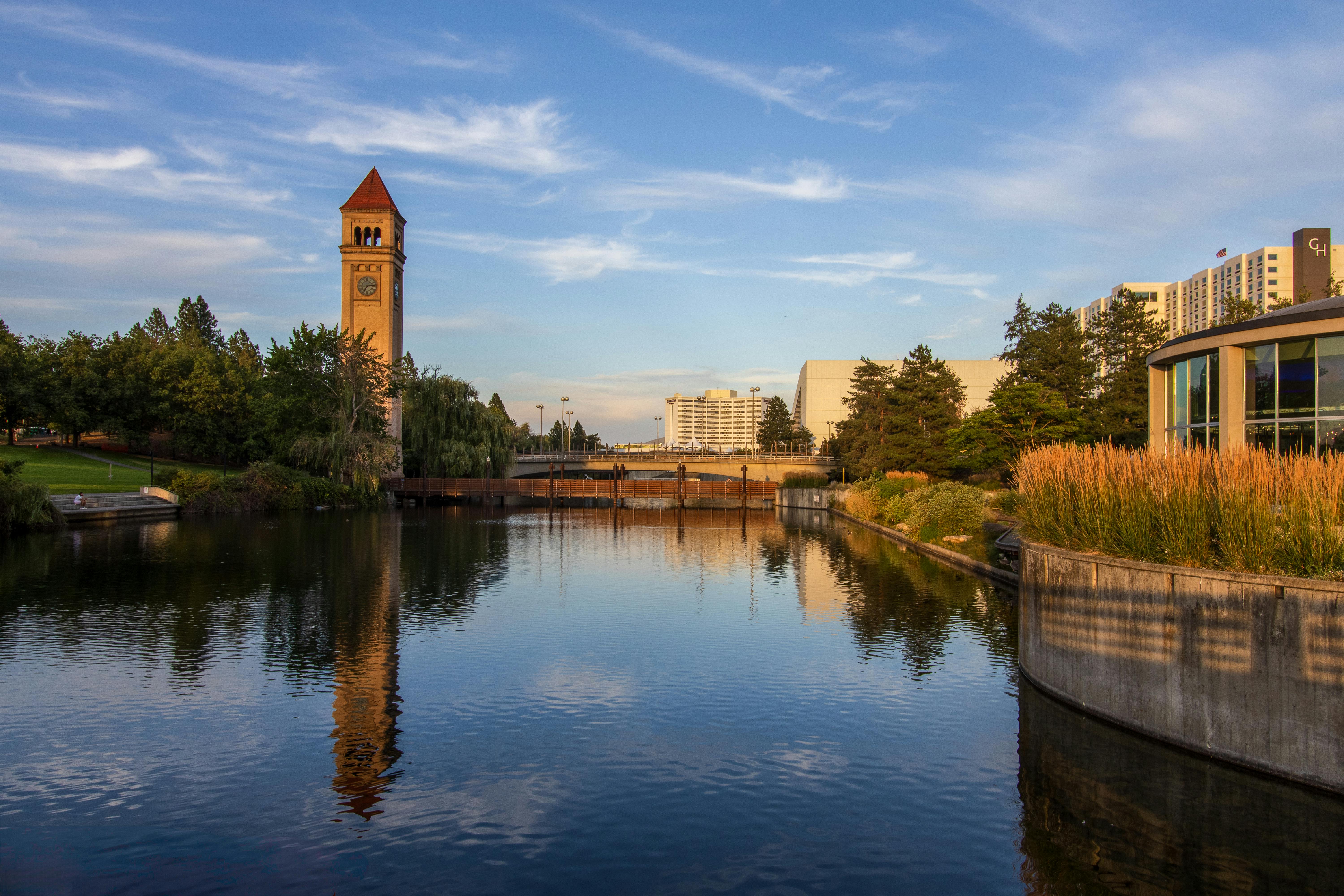 A tranquil riverfront scene featuring the iconic Spokane Clocktower and lush greenery, perfect for travel inspiration.