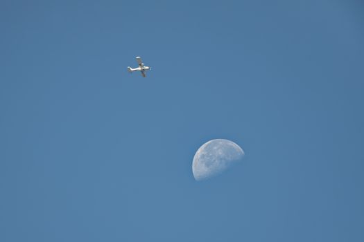 A small aircraft soaring in the clear sky with a visible crescent moon, symbolizing flight and tranquility.