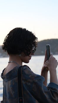 Woman taking a photo with smartphone near the sea during sunset.