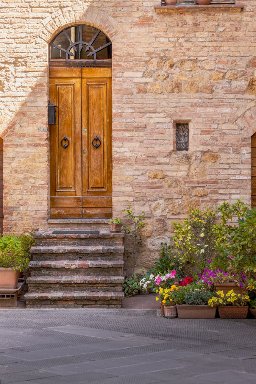 A tall wooden door in a limestone facade, potted flowers along the step