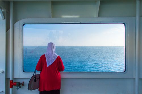 Free A woman gazing out the window of a cruise ship at the serene sea horizon. Stock Photo