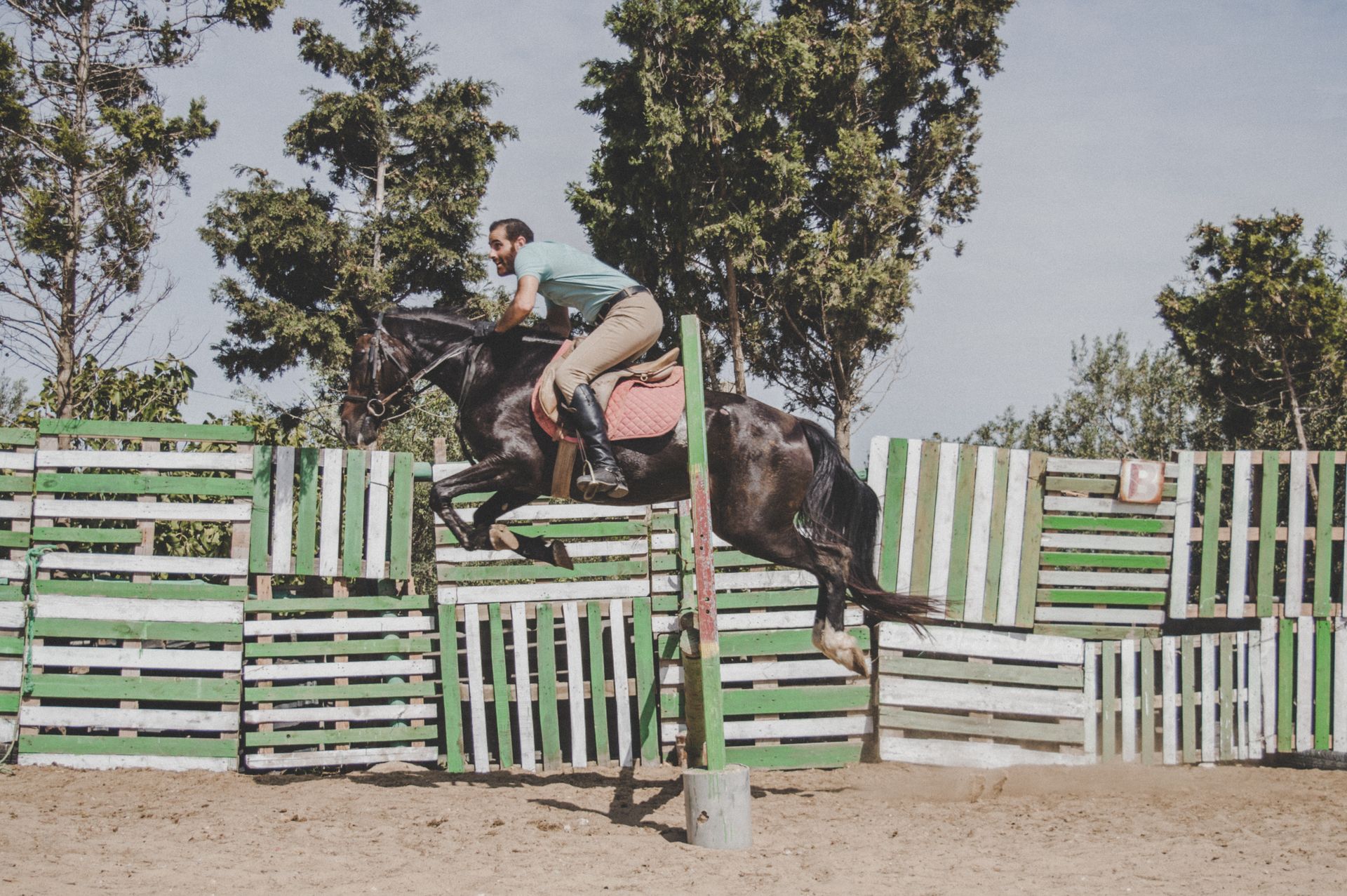 A man riding a horse jumps over a painted fence during an equestrian event in an outdoor arena.