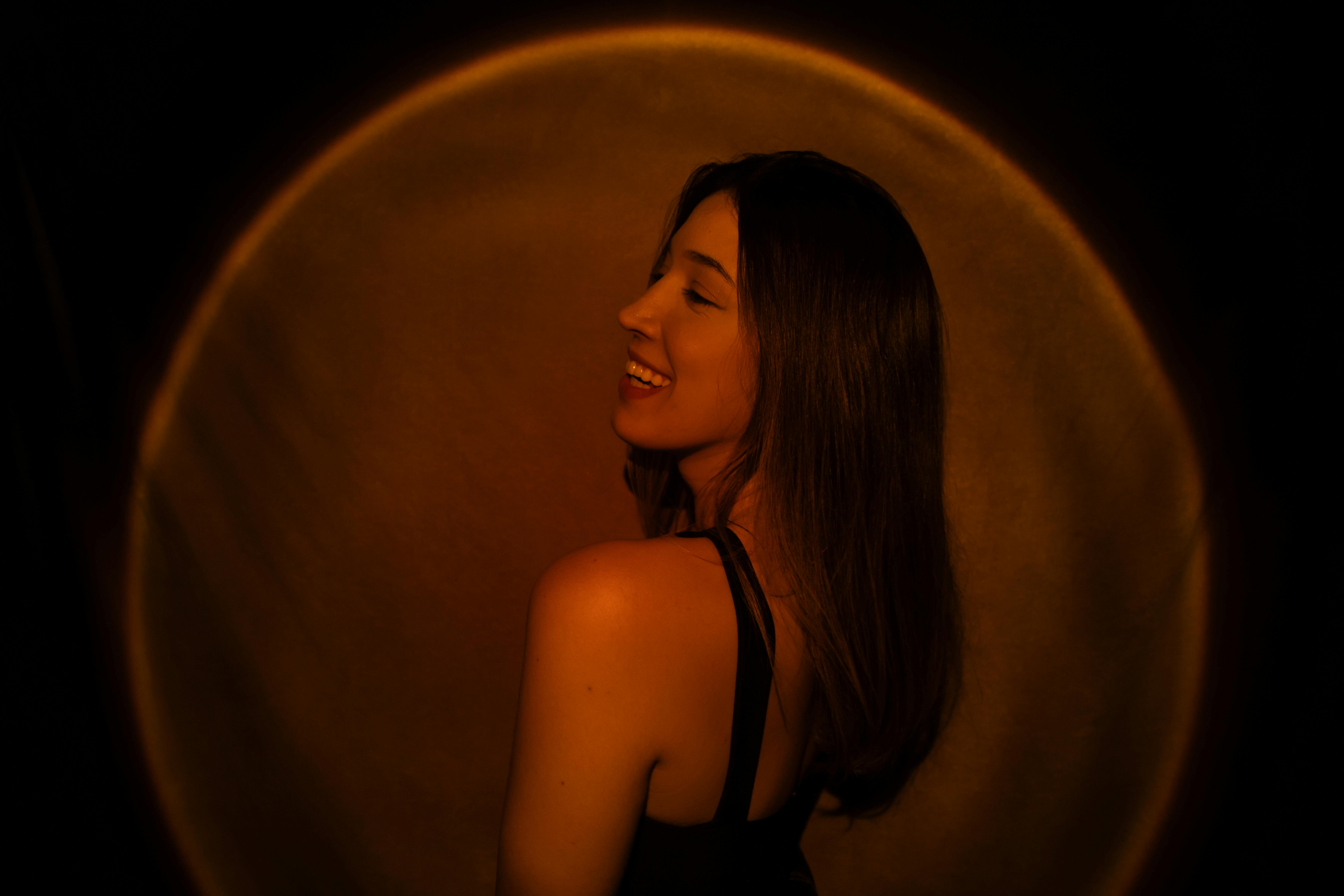 a woman in a black dress is smiling in front of a yellow light