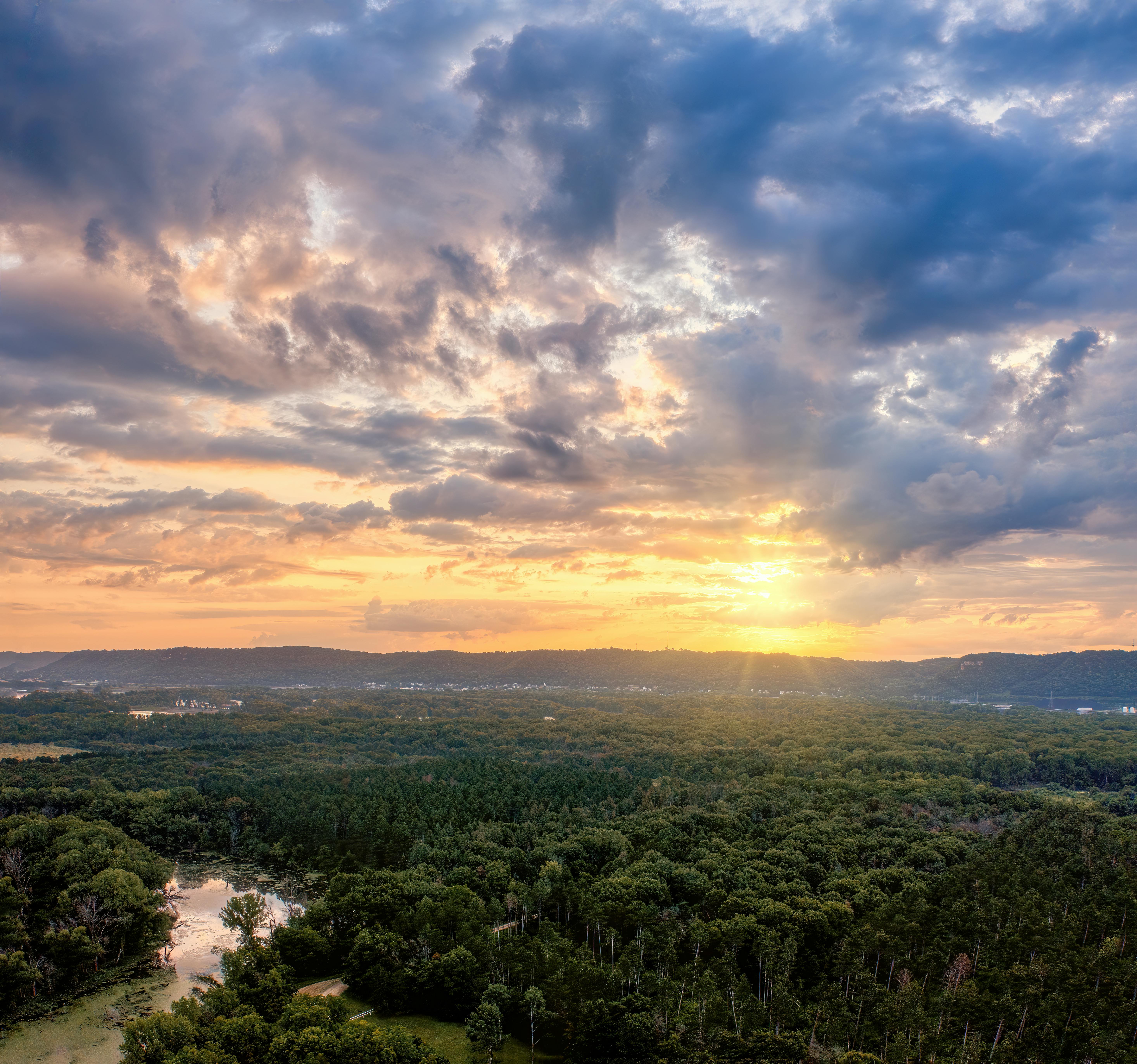 the sun sets over a valley with trees and clouds