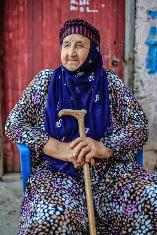 Free Portrait of an elderly woman in traditional attire sitting outdoors in Diyarbakır, Türkiye, holding a walking stick. Stock Photo