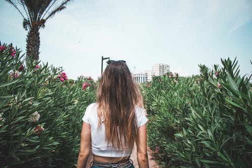 Back view of a Woman Wearing a White Crop top  in Between Flower  Plants