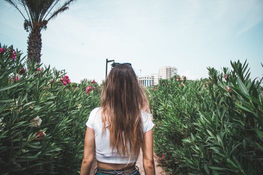 一位身着白色露脐上衣的女士，走过种满鲜花和绿植的郁郁花园