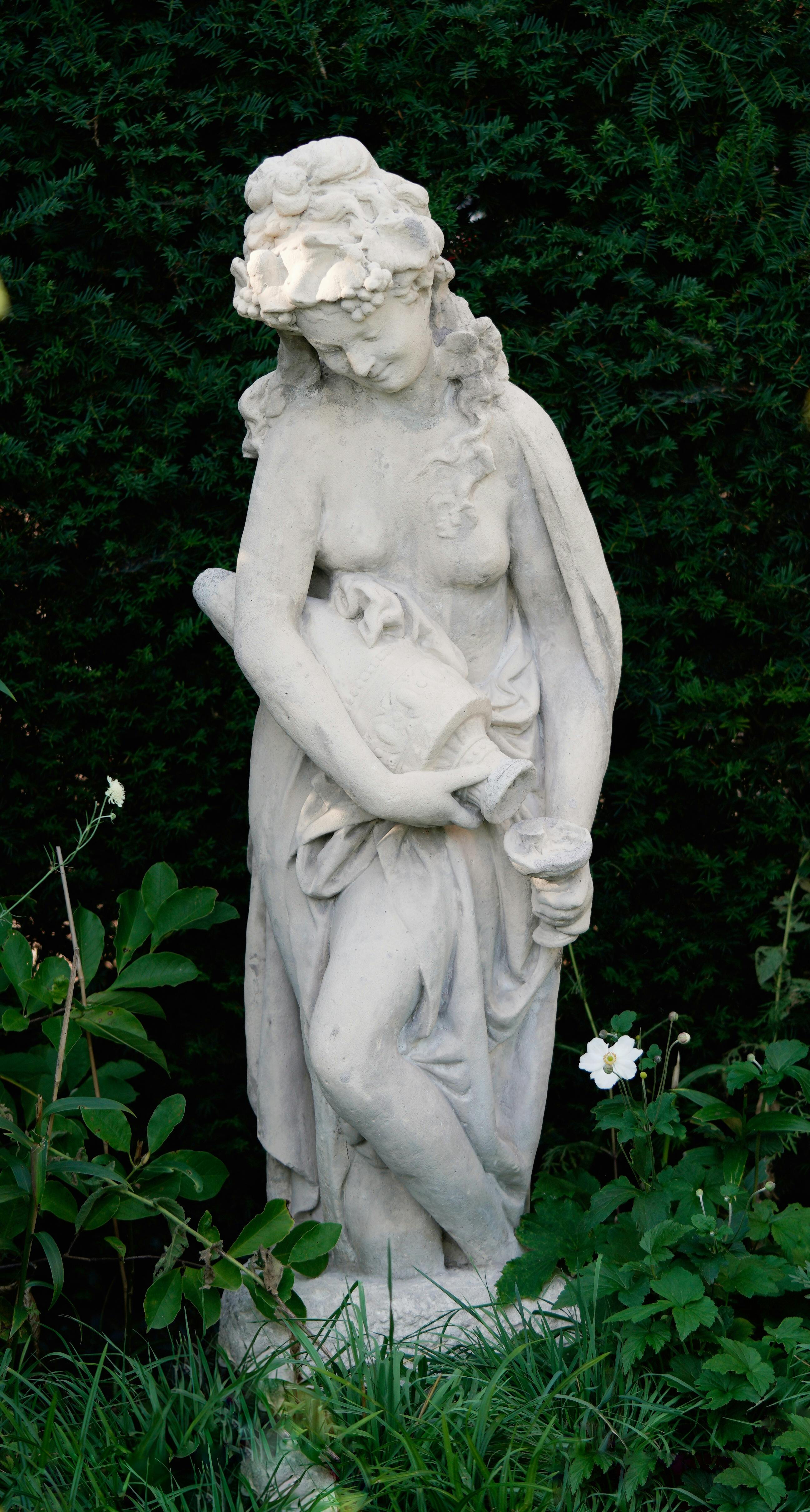 Elegant marble statue set against lush greenery, embodying mythological grace.