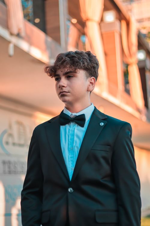 Free Portrait of a young man in a suit and bow tie in an outdoor setting with warm lighting. Stock Photo