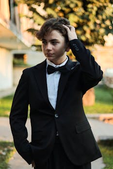 A young man in a black suit adjusting his hair confidently outdoors.