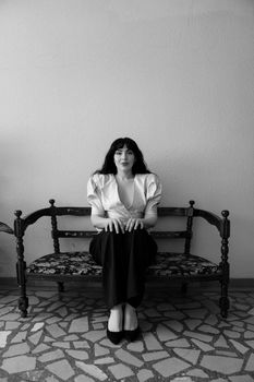 Black and white portrait of a woman sitting elegantly on a vintage chair indoors.