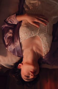 A woman in a satin robe and lace dress lies gracefully indoors.