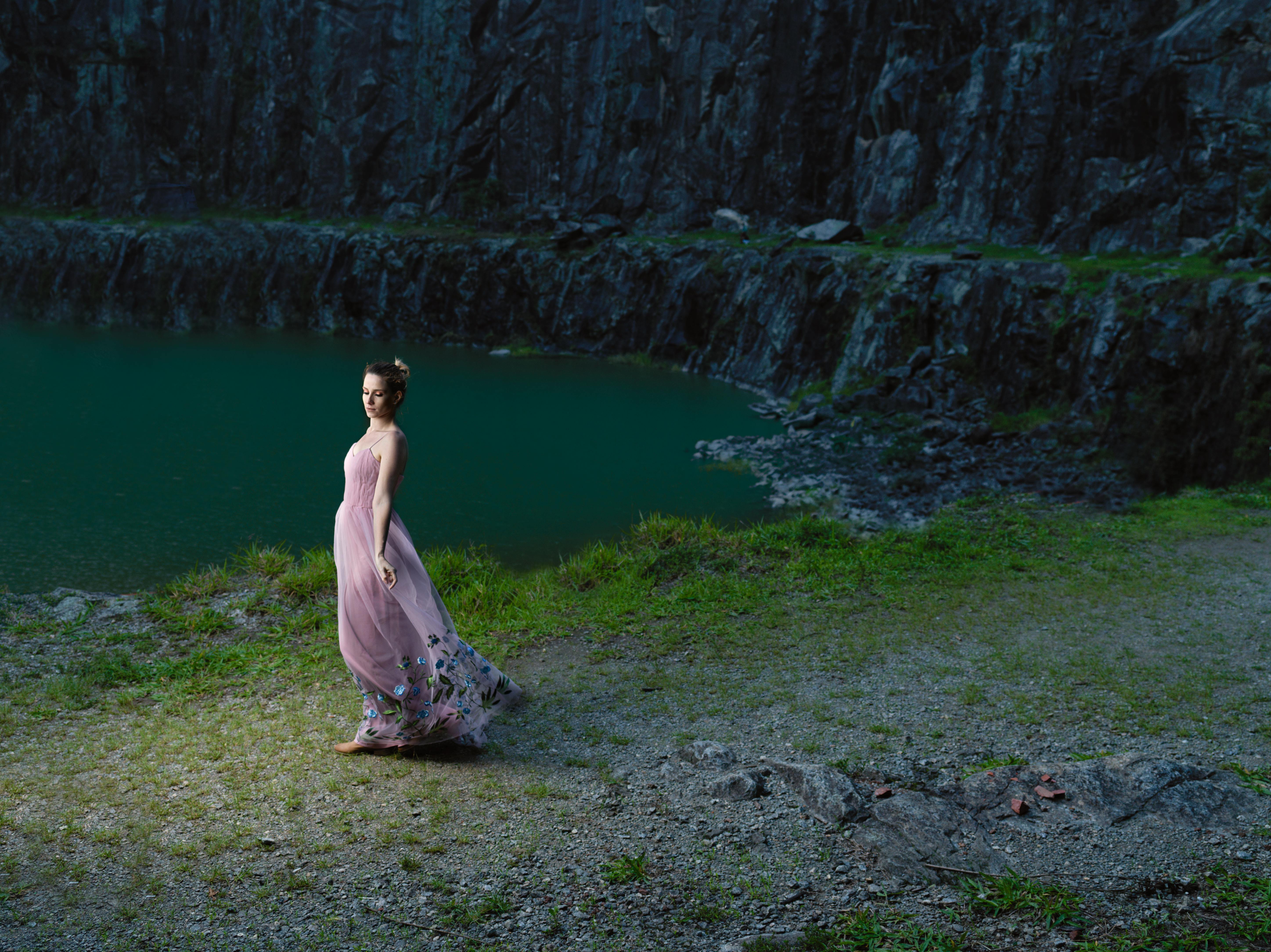 a woman in a pink dress standing near a lake