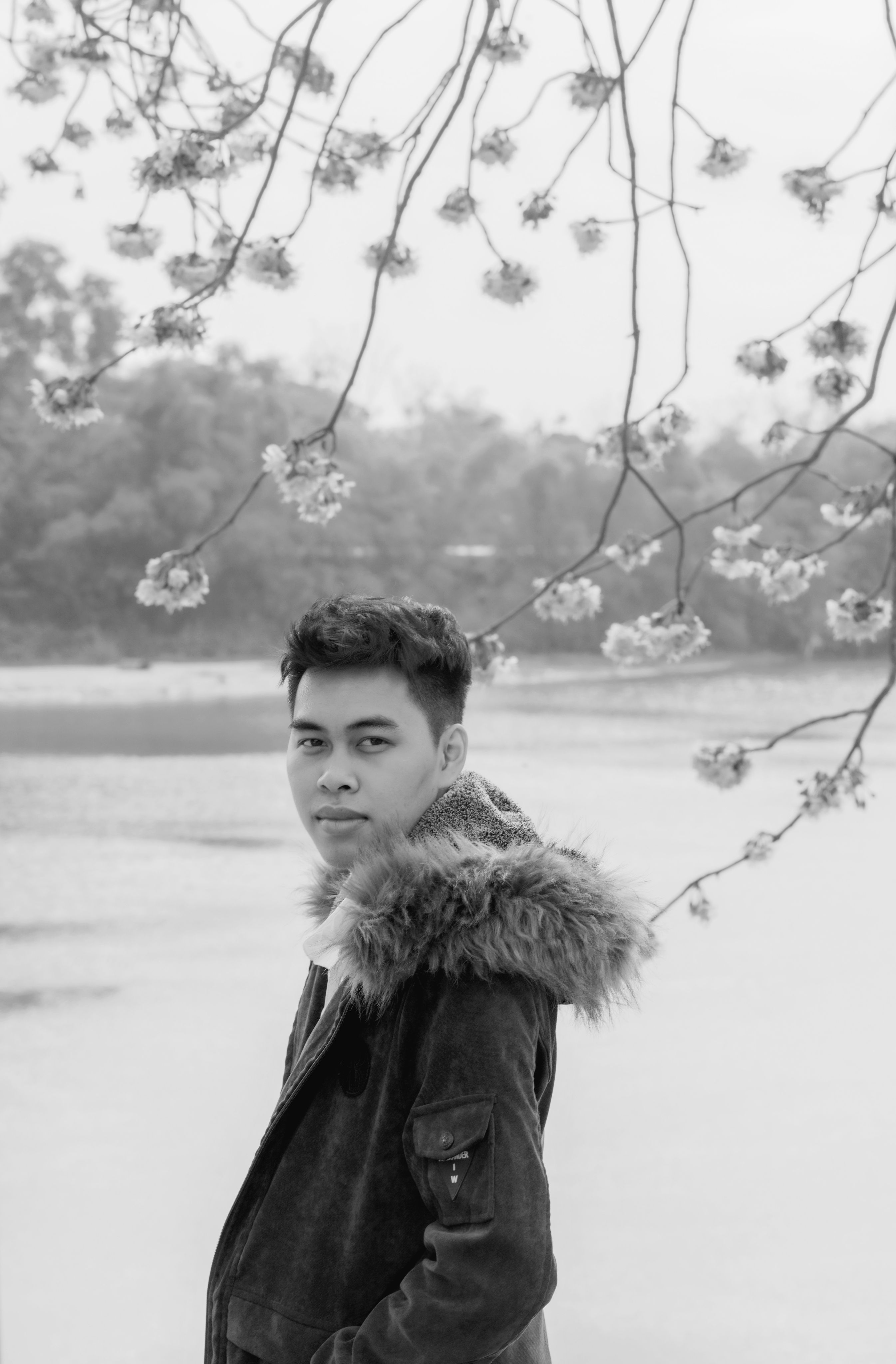Black and white portrait of a man in a coat by a lake, surrounded by winter branches.