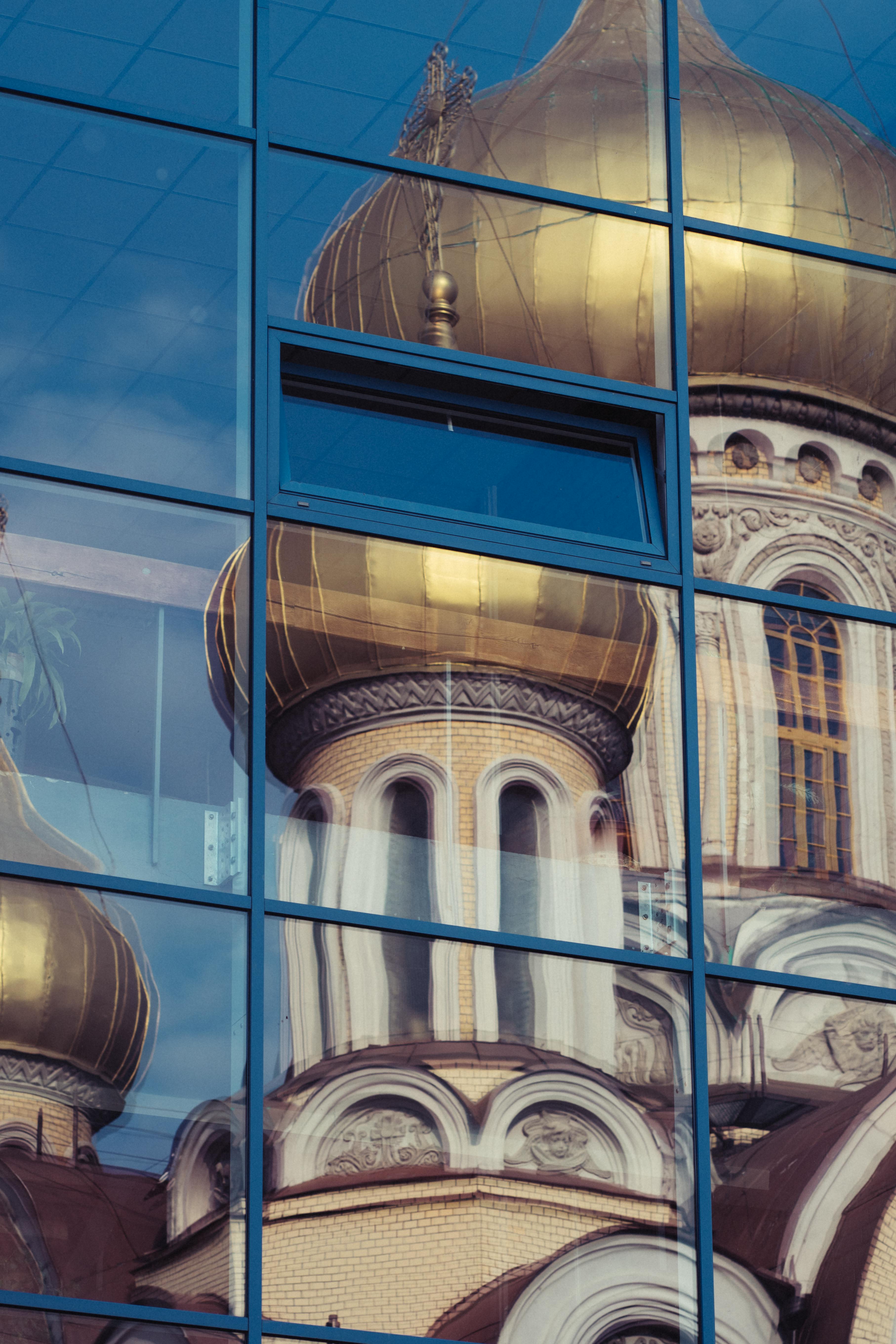Golden domes of Vilnius Cathedral reflected in a modern glass facade.