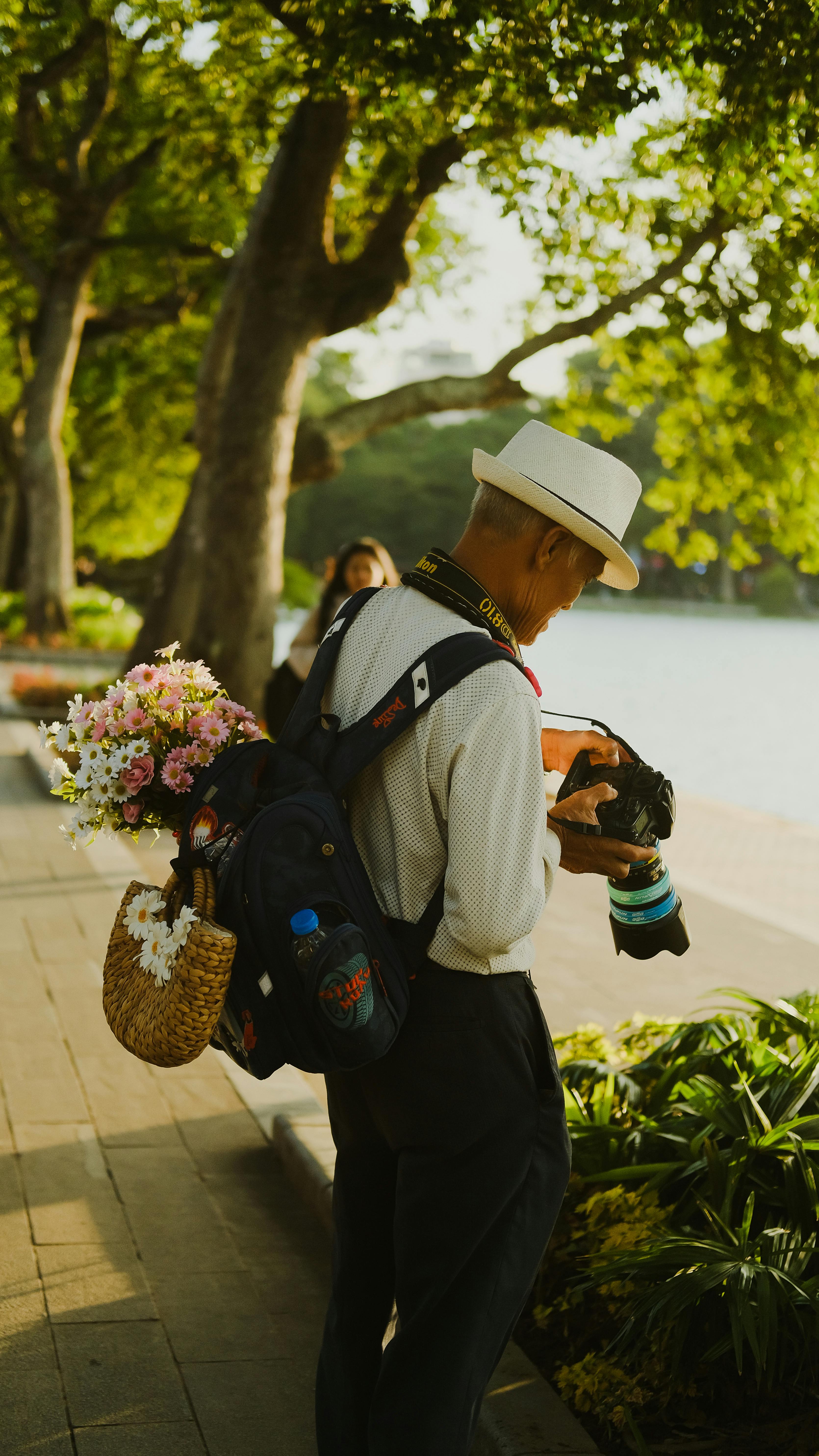 Elderly man selling flowers on a sunny street near a lake in Hanoi, Vietnam, showcasing everyday life.