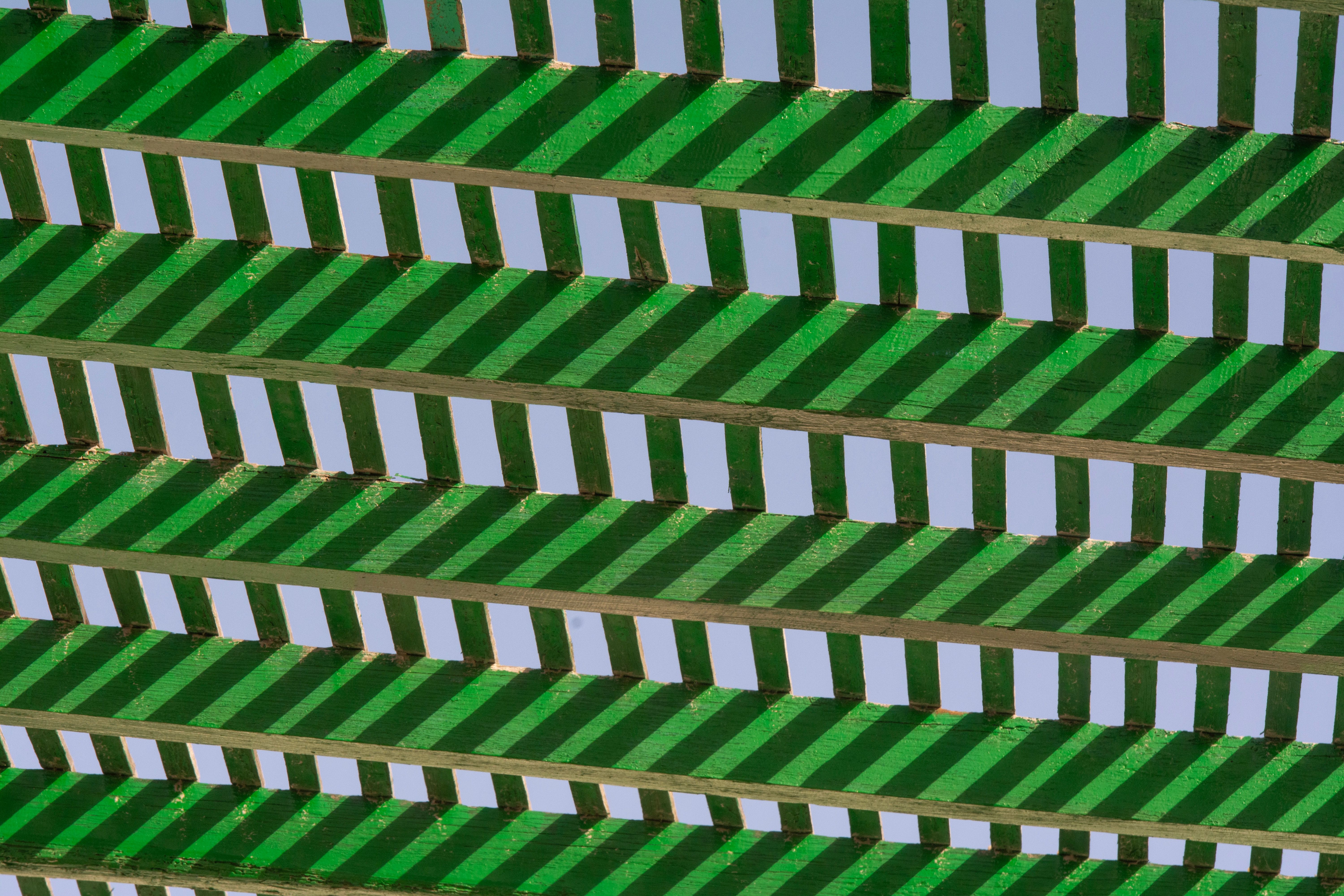 Abstract image of green pergola slats creating a geometric shadow pattern.