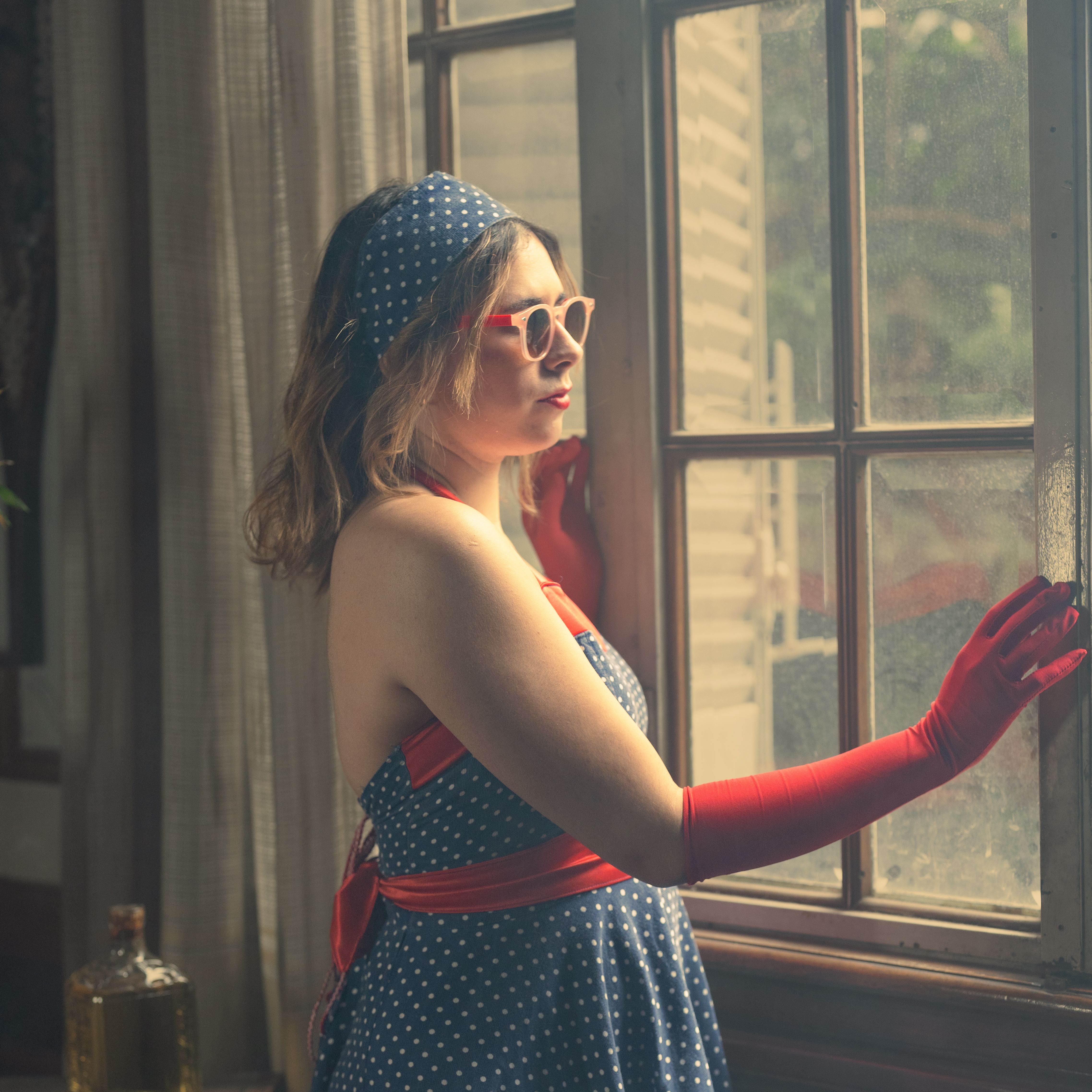A woman in a polka dot dress and red gloves looking out a window