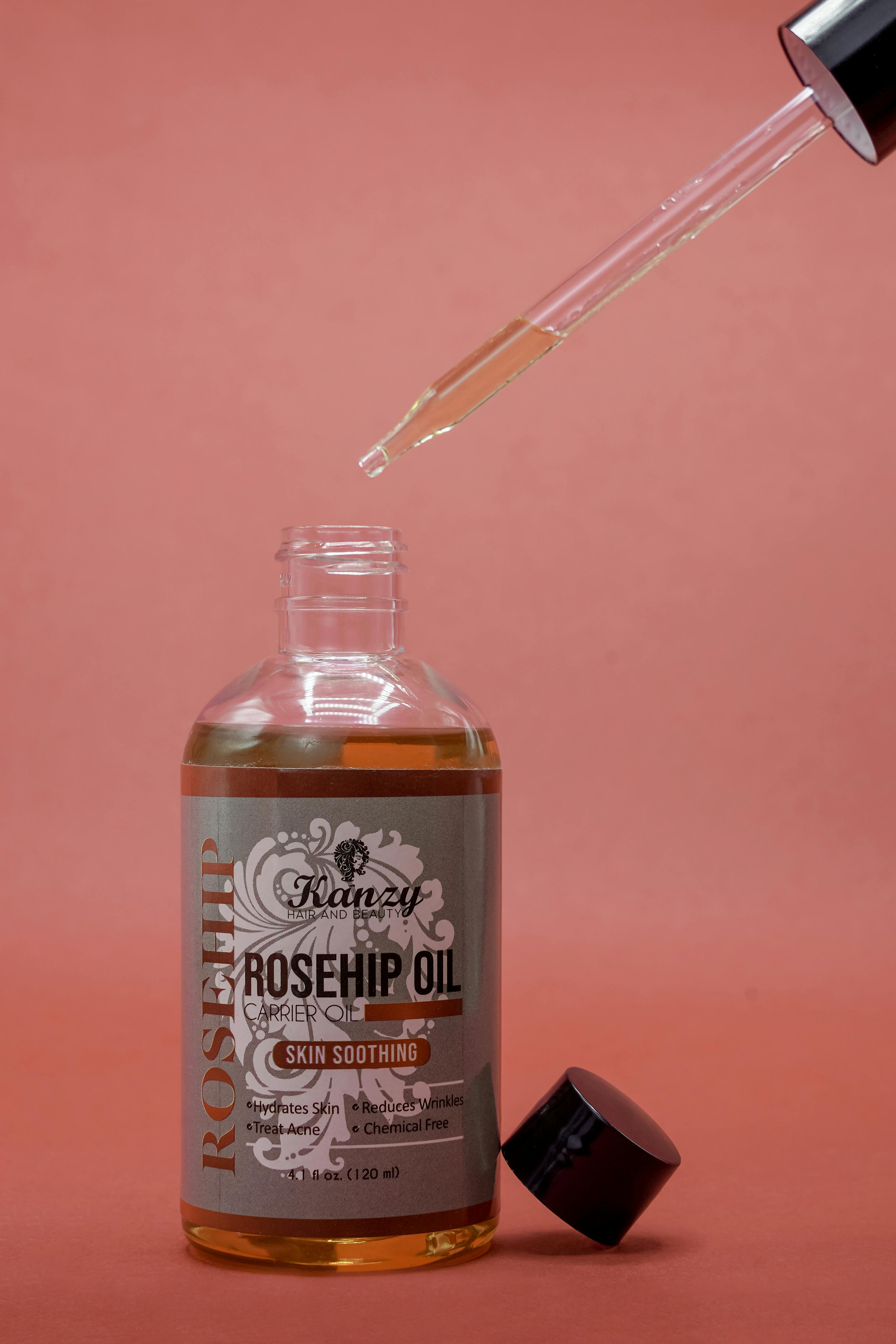 A bottle of Kanzy Rosehip Oil with an eyedropper against a pink background.