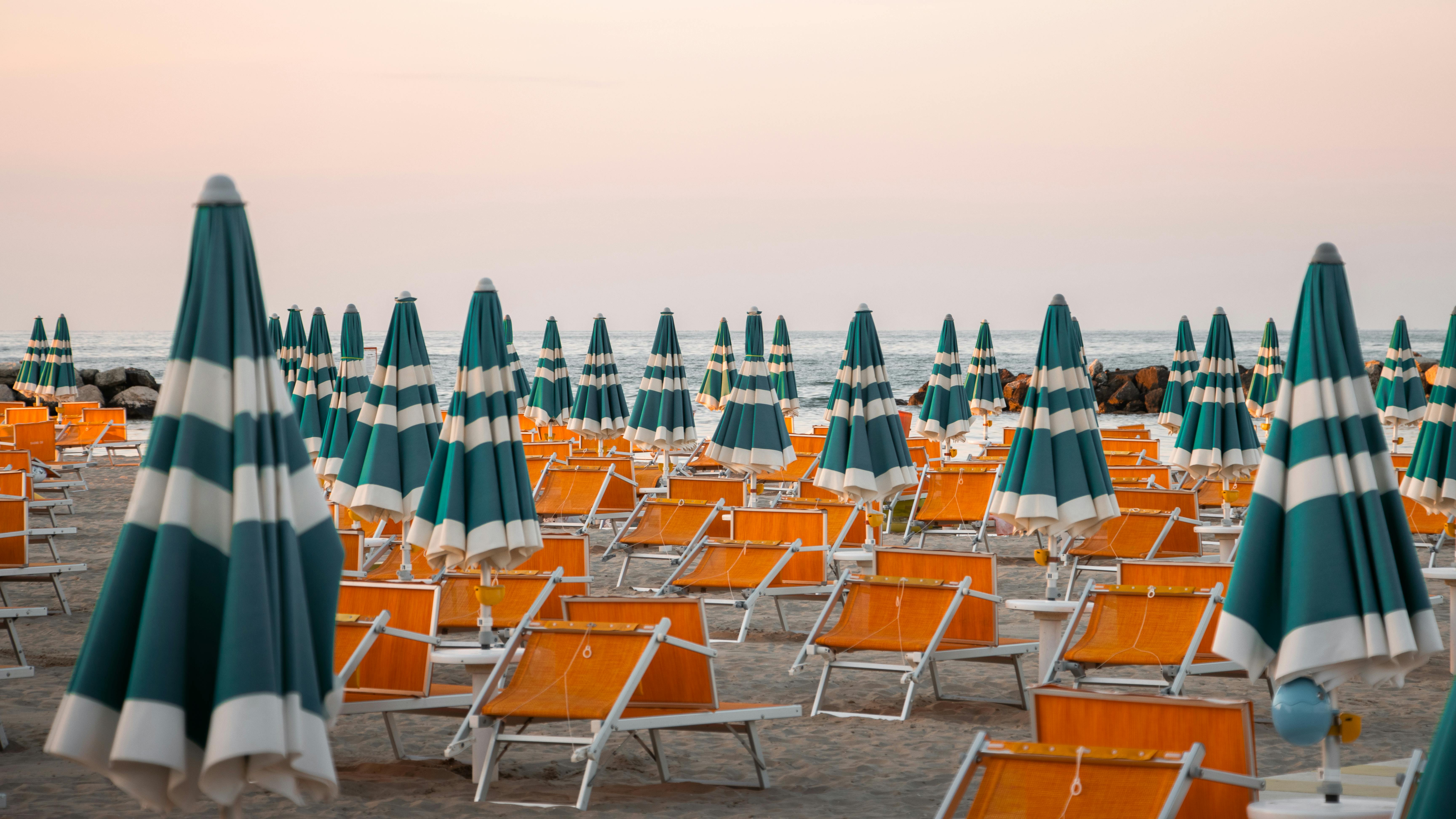 Colorful striped umbrellas and chairs on Rimini beach during sunset, perfect for summer vibes.