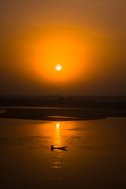 A lone boat silhouette at sunset on calm waters, creating a peaceful reflection.